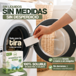 Mano introduciendo una tira de detergente VAMZ en la lavadora, junto a su caja y las indicaciones de disolución en agua fría o caliente.